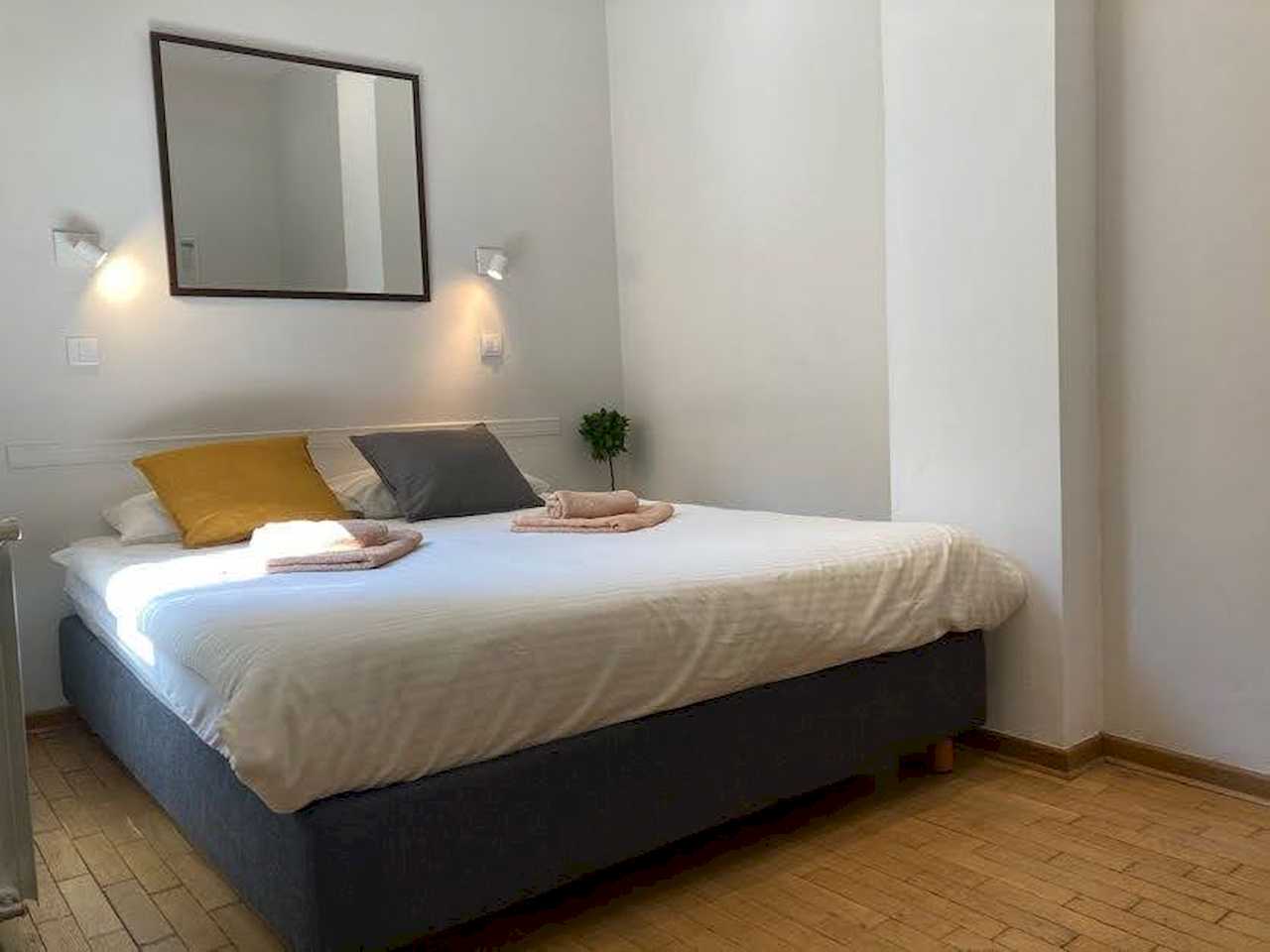 Spavaća soba sa bračnim krevetom, ogledalom iznad uzglavlja i zidnim lampama – Apartman Trg 2 – City Break Apartments