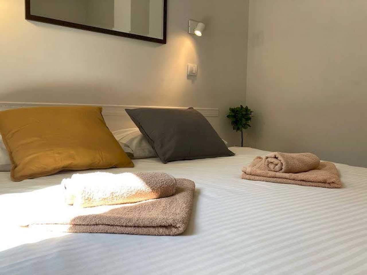 Detalj bračnog kreveta sa peškirima, ukrasnim jastucima i lampom za čitanje – Apartman Trg 2 – City Break Apartments
