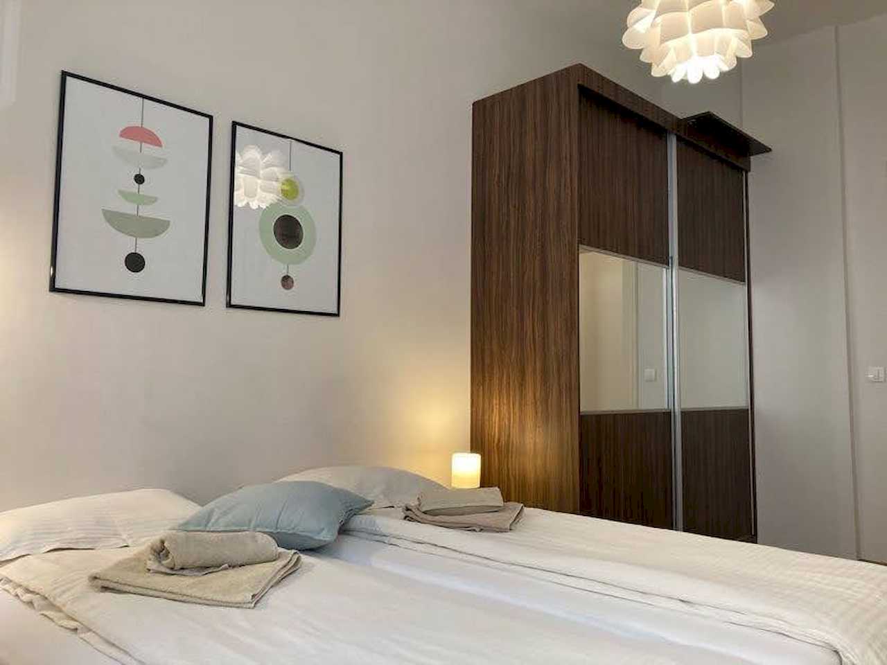 Spavaća soba sa bračnim krevetom, tamnim ormarom sa ogledalima i apstraktnim slikama – Apartman Trg 2 – City Break Apartments