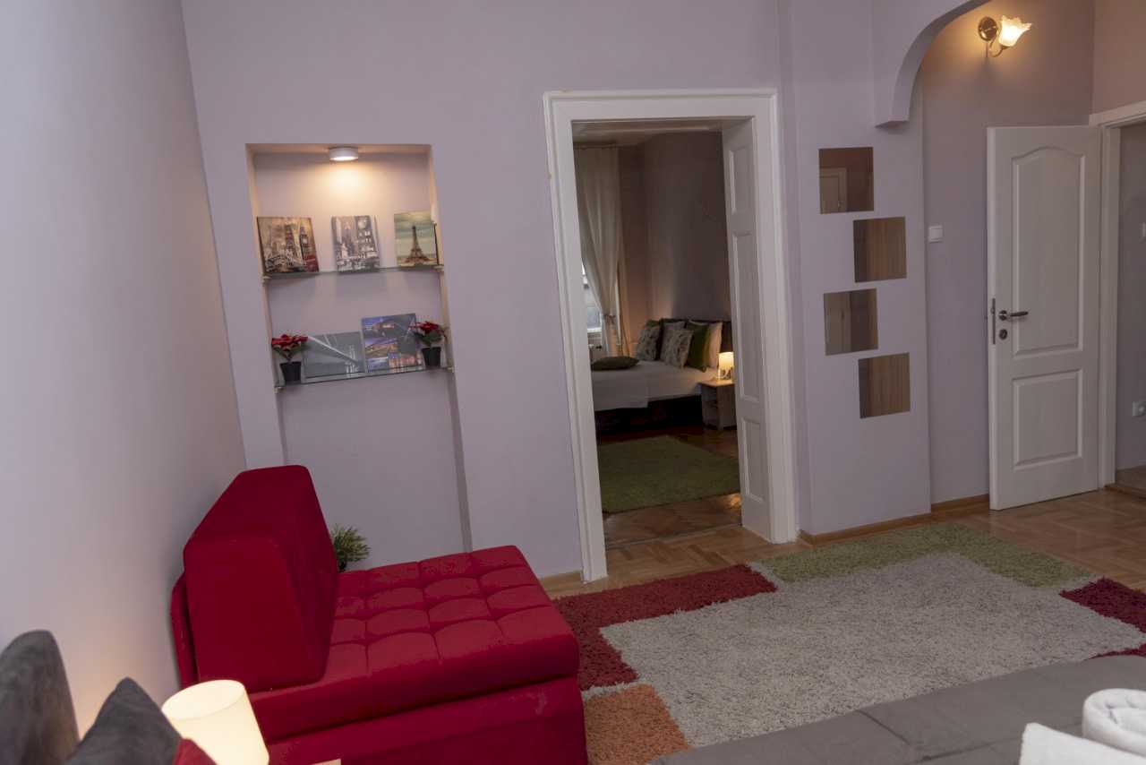 Četvorosobni stan Trg 4 (Kolarčeva, Beograd) – dnevni boravak sa crvenom foteljom, nišom sa policom i pogledom na spavaću sobu