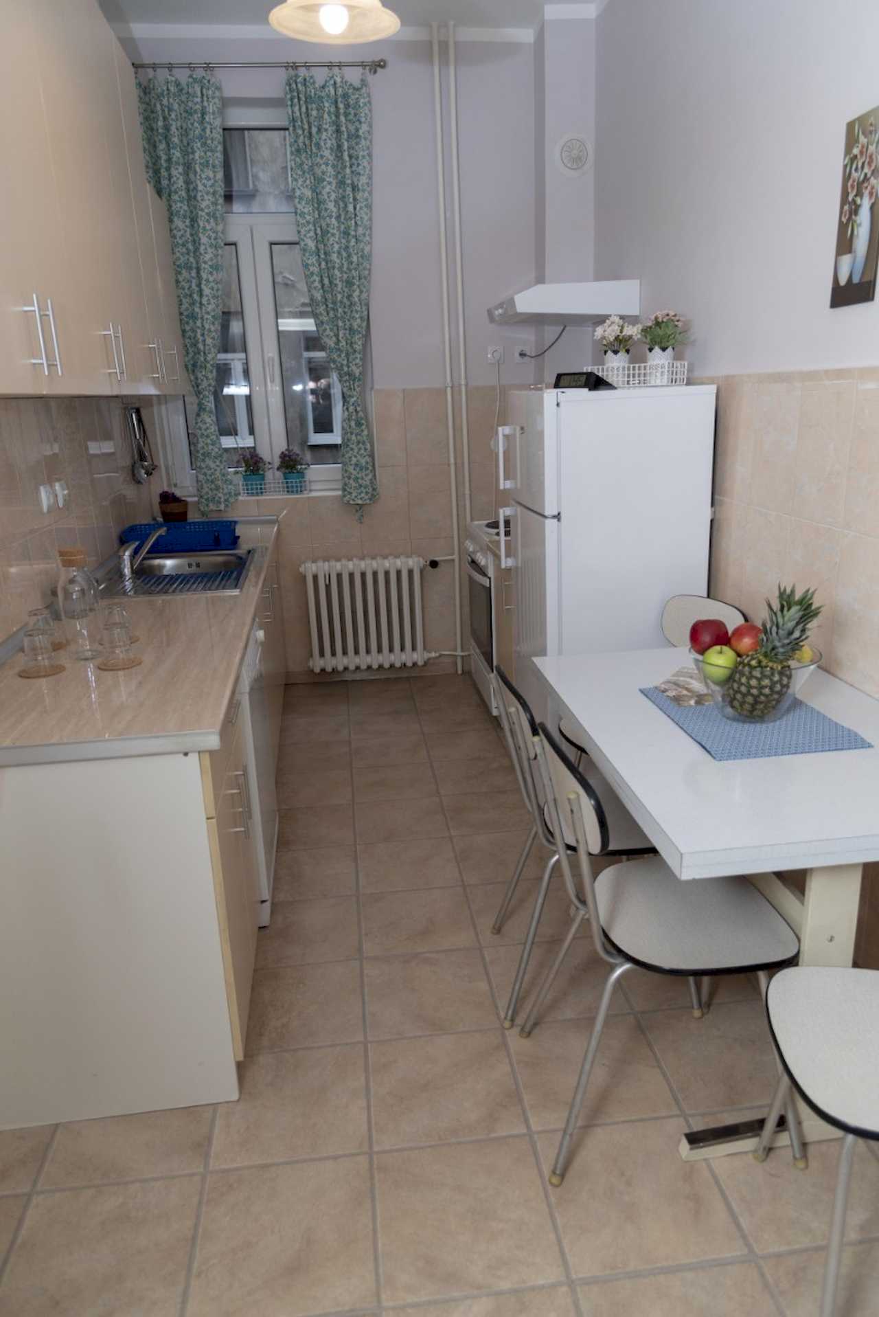 Četvorosobni stan Trg 4 (Kolarčeva, Beograd) – kuhinja sa krem elementima, belim frižiderom i malim trpezarijskim stolom