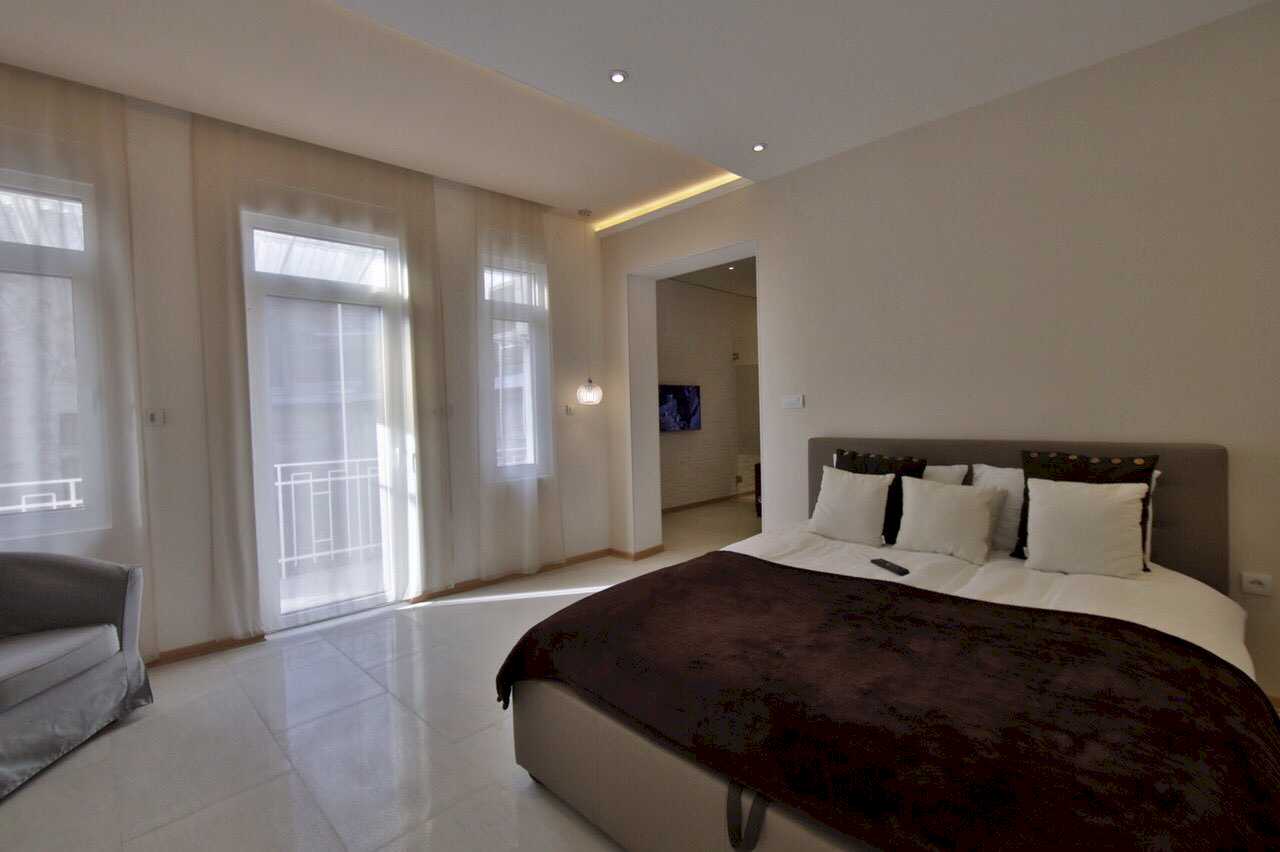 Apartman Twin 1 (Carice Milice, centar Beograda) – spavaća soba sa bračnim krevetom, francuskim balkonom sa zavesama i sivom foteljom u uglu