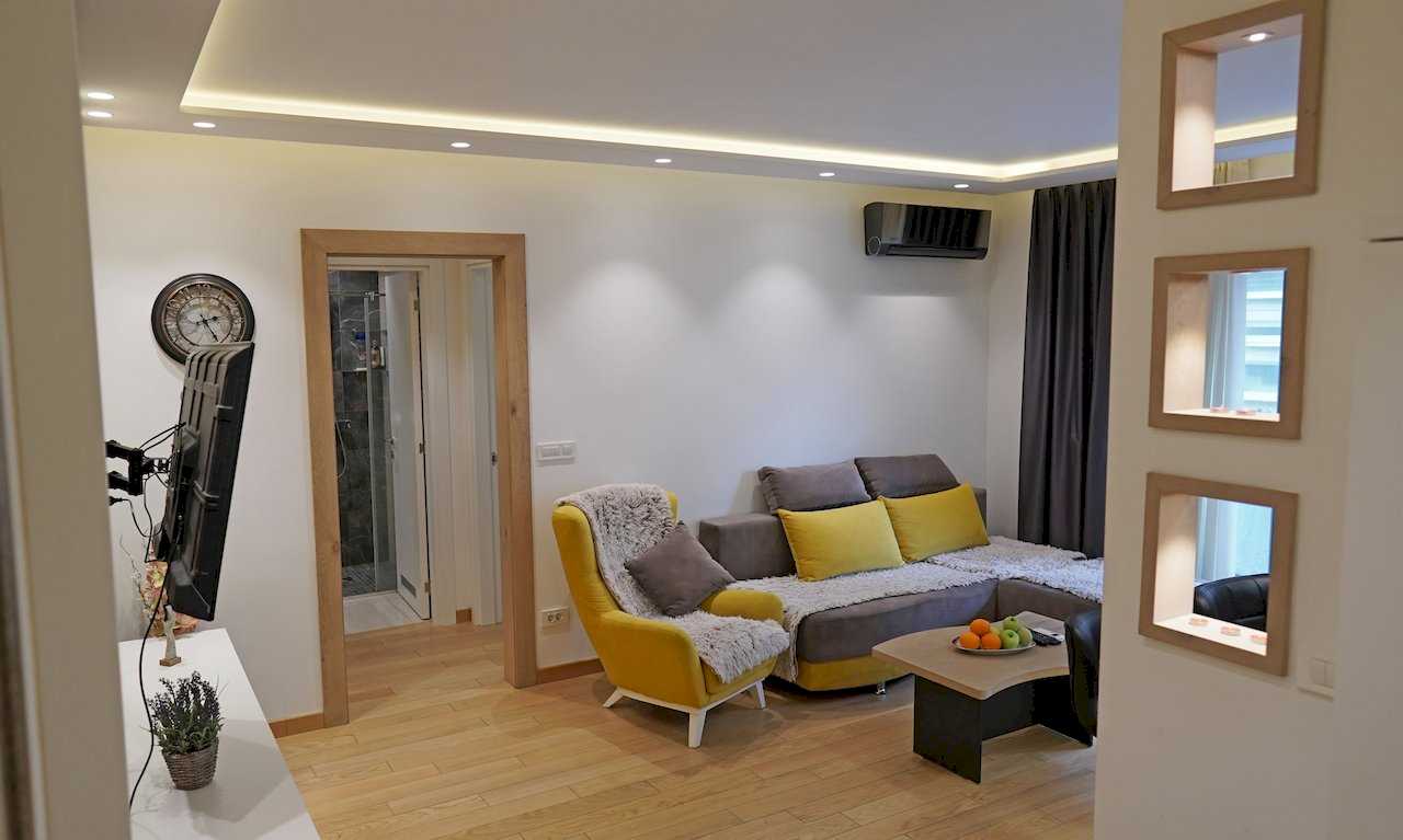 Apartment Vuk (Vuk's Monument, Belgrade) – living room with grey corner sofa, yellow armchair and wall-mounted TV