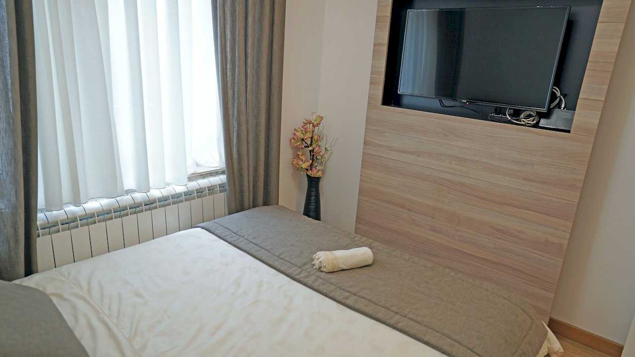 Apartment Vuk (Vuk's Monument, Belgrade) – bedroom with double bed, TV in wood panel and window with curtains
